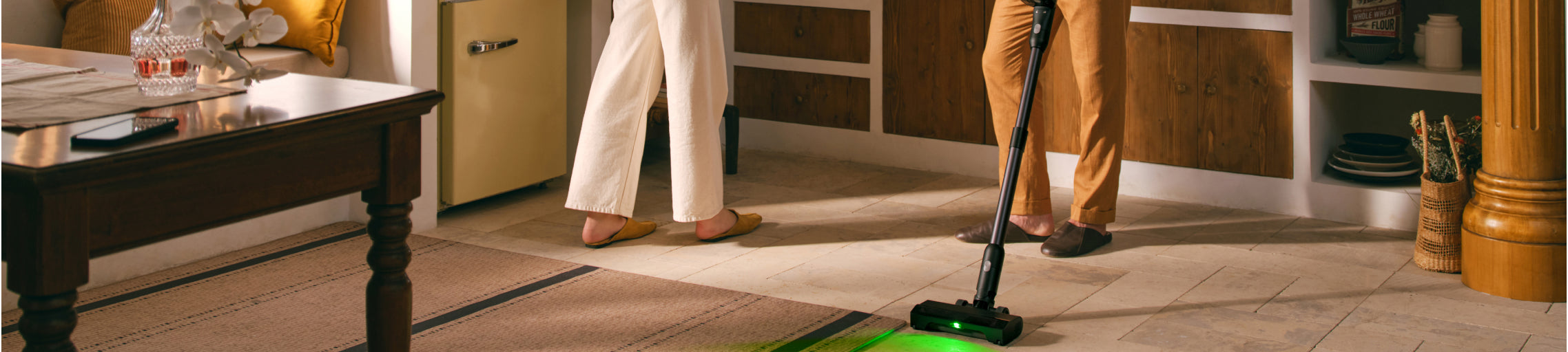 A person using a black Roborock cordless stick vacuum on a living room rug, with a green light illuminating the dust on the floor