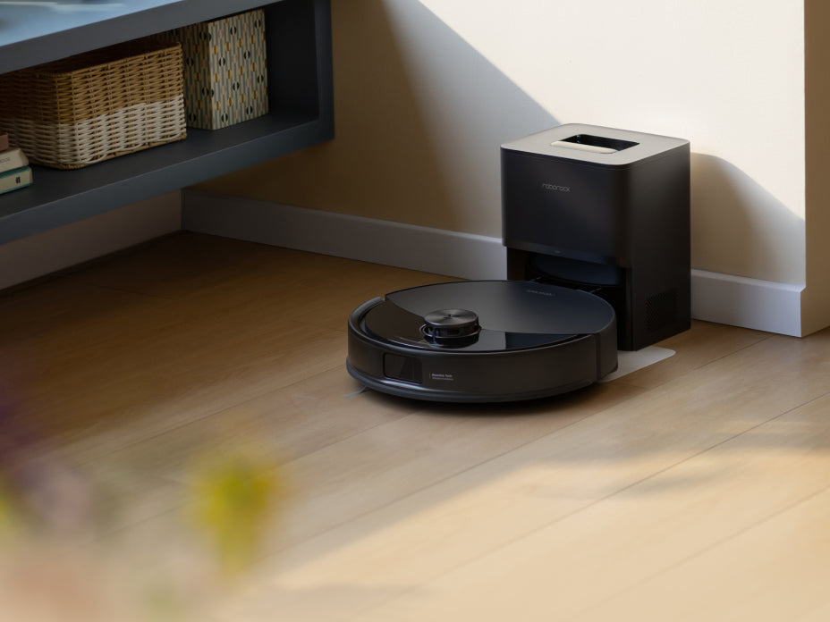 Black Roborock Q10 S5+ robot vacuum docked in a black base station on a light wooden floor