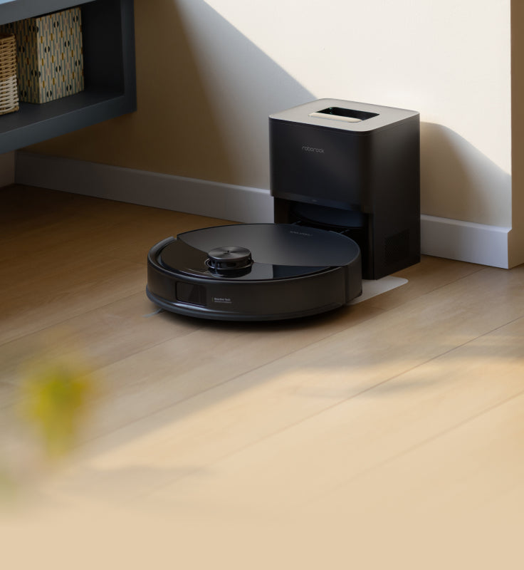 Black Roborock Q10 S5+ robot vacuum docked in a black base station on a wooden floor